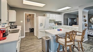 Una cocina moderna con armarios blancos, una isla central con taburetes altos y un refrigerador grande.