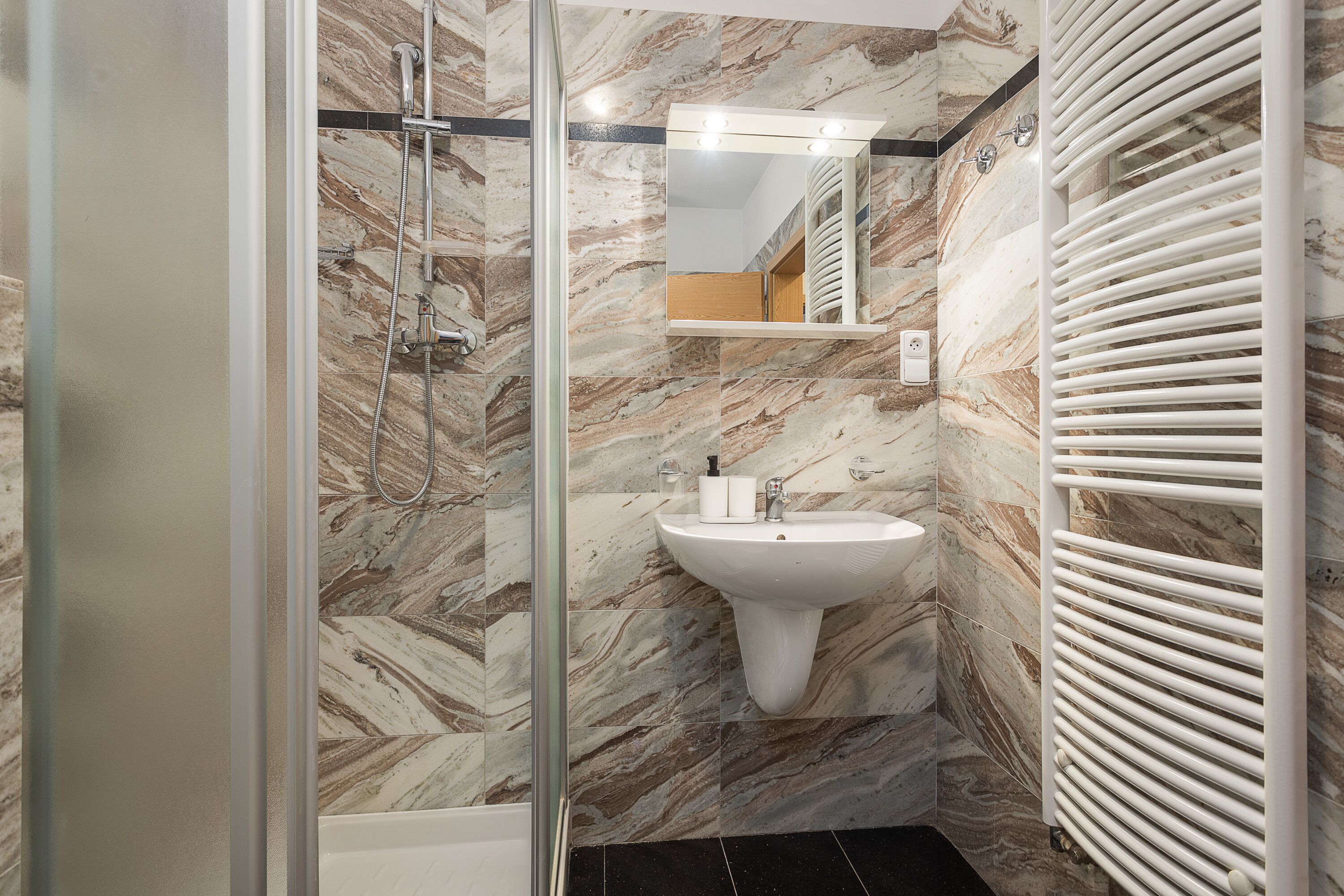 A bathroom with a glass shower enclosure, a pedestal sink, and a white towel rack.
