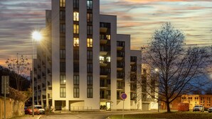 En moderne bygning med flere etager, altaner, et parkeringsforbudsskilte og et træ i forgrunden.