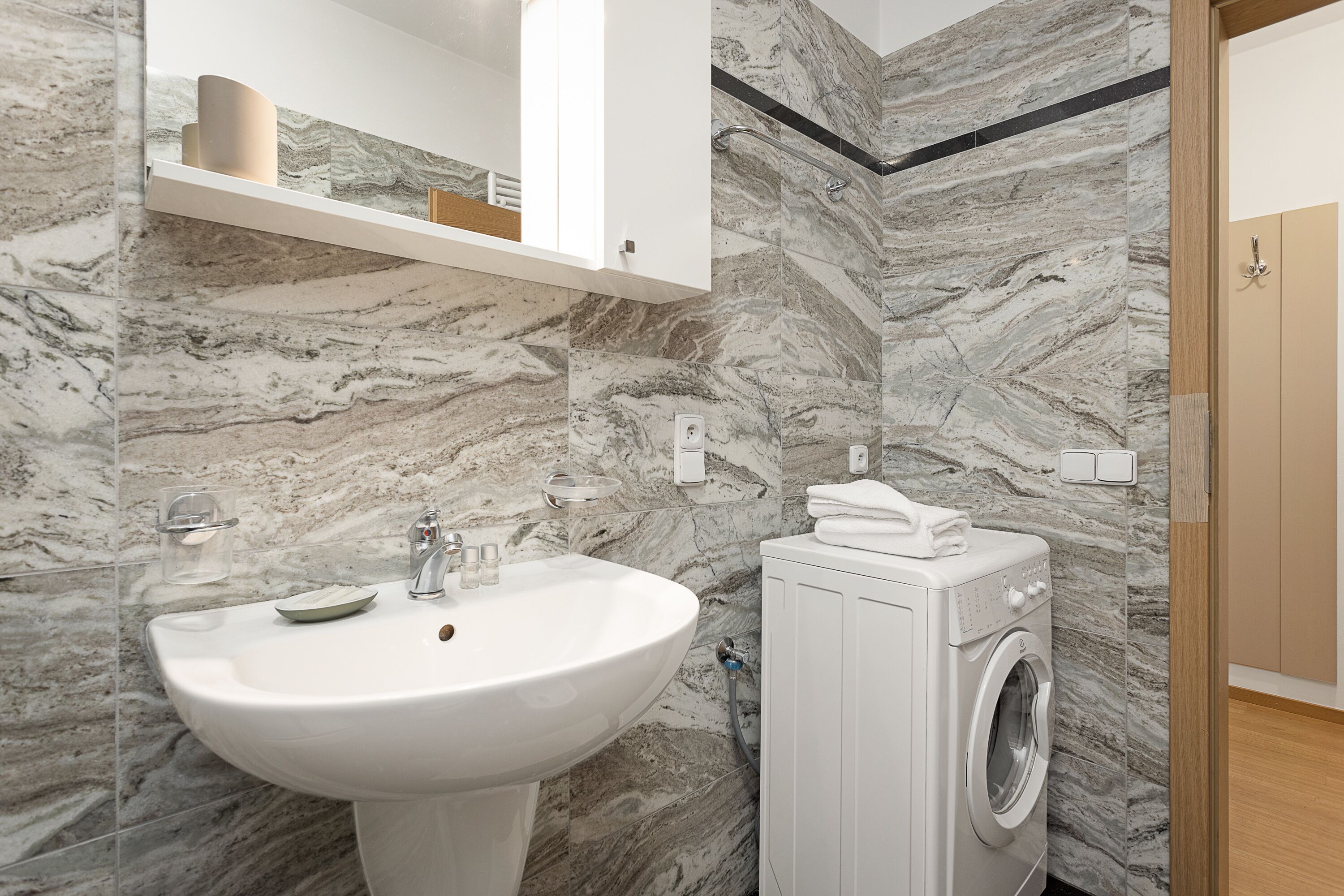 Une salle de bain avec un pare-feu en marbre, un lavabo blanc et un lave-linge à chargement frontal.