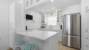 A modern kitchen with white cabinetry, a stainless steel refrigerator, and a central island with bar stools.