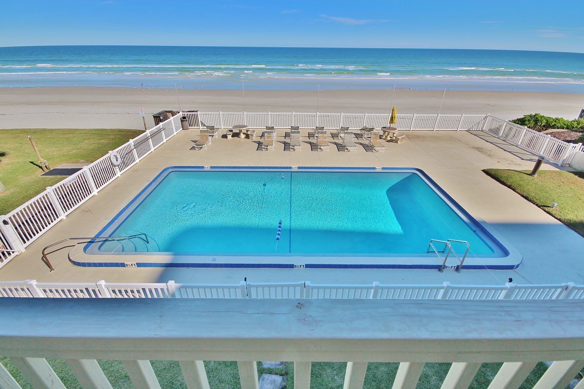 A rectangular pool with a white deck and a white fence.
