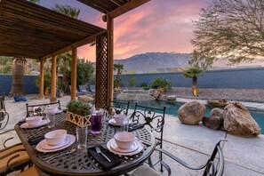 A table set for dining with a view of a pool and mountains.