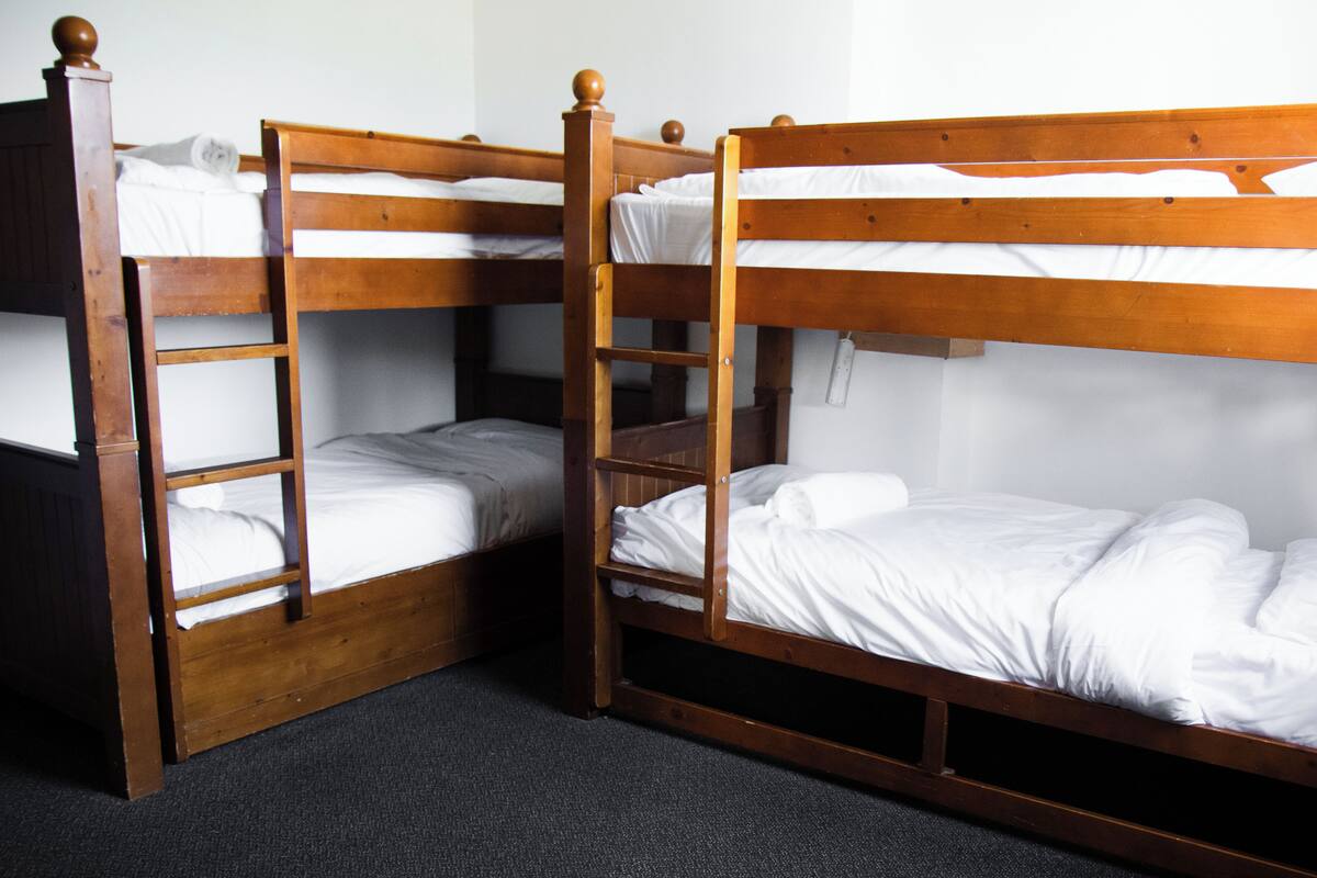 Une chambre avec deux lits superposés en bois, chacun équipé d’une échelle et d’un matelas.