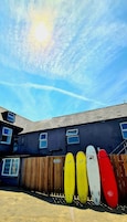 A row of surfboards against a building with a wooden fence and a clear sky.