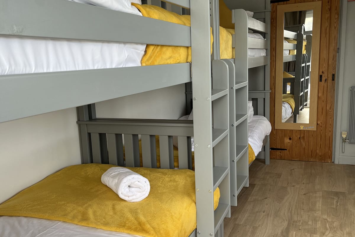 Une chambre avec un lit superposé, un plancher en bois et une porte dotée d’un miroir.