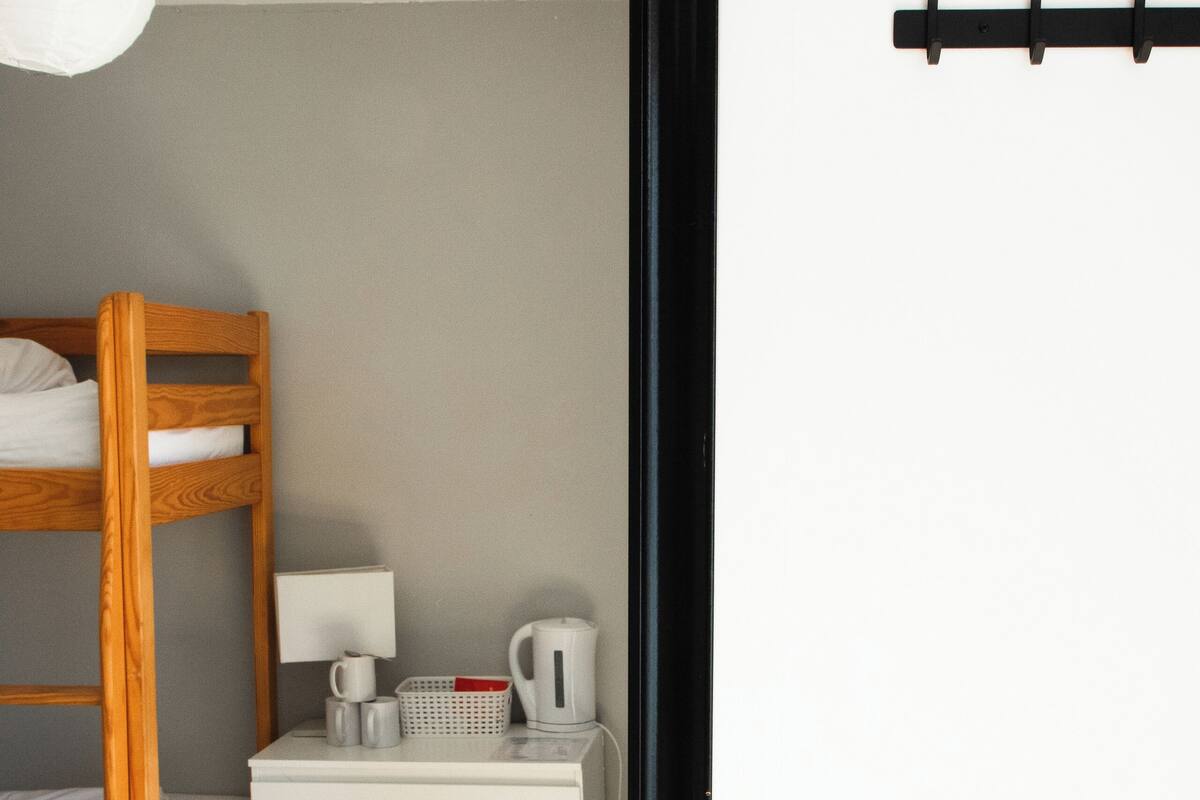 Un lit superposé avec une table de chevet, une lampe et une bouilloire.