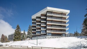 Ein mehrstöckiges Gebäude mit Balkonen, umgeben von schneebedeckten Bäumen und wolkenlosem Himmel.