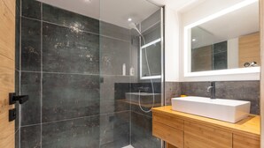 Un baño moderno con ducha de vidrio, lavabo blanco y tocador de madera.