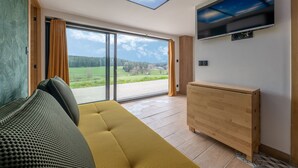 Una habitación moderna con sofá, un mueble de madera y un ventanal con vistas a un paisaje verde.