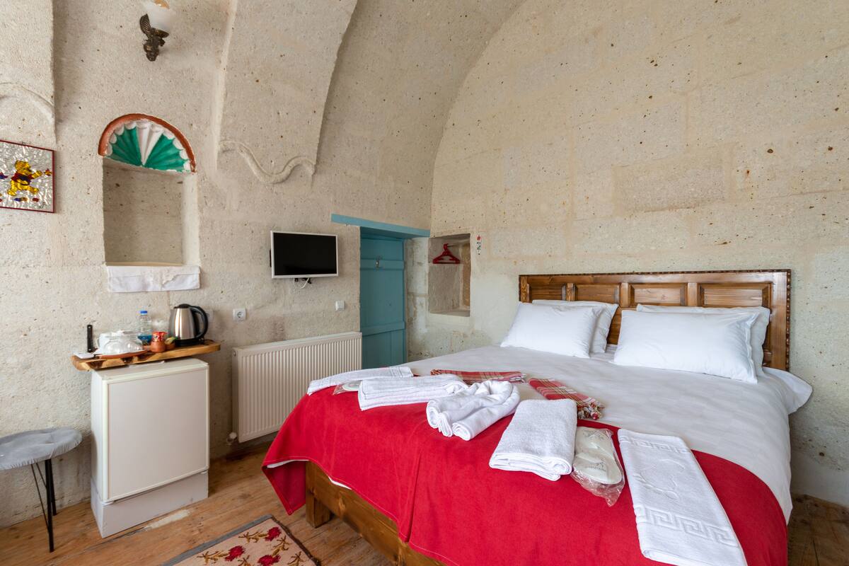 Een gezellige slaapkamer met een houten bed, een klein wit bureau, een televisie en een rode spreideken.
