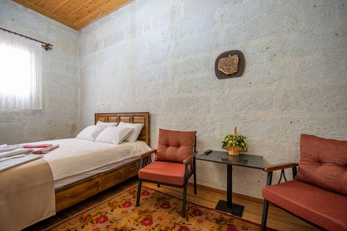 Een slaapkamer met een bed, een houten stoel, een klein tafeltje en een decoratief wandpaneel.
