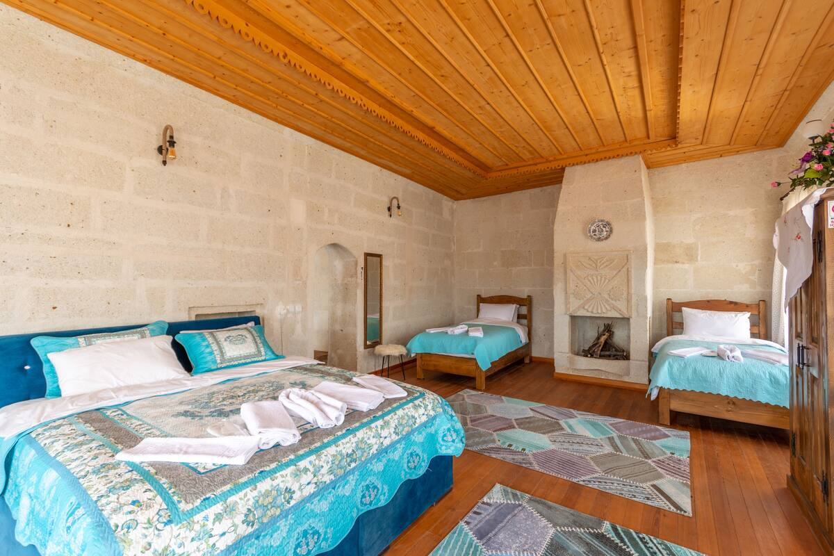 Een slaapkamer met twee bedden, houten balken in het plafond, stenen muren en een kleine open haard.
