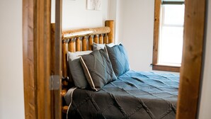 Una cama con cabecera de madera y varios almohadones, una ventana con luz natural y un marco de puerta.
