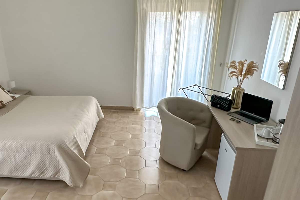 A hotel room with a bed, a desk with a laptop, a chair, and a window with curtains.