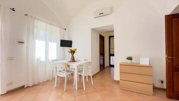 Um quarto claro com uma mesa de jantar, cadeiras, uma televisão e um aparador de madeira.