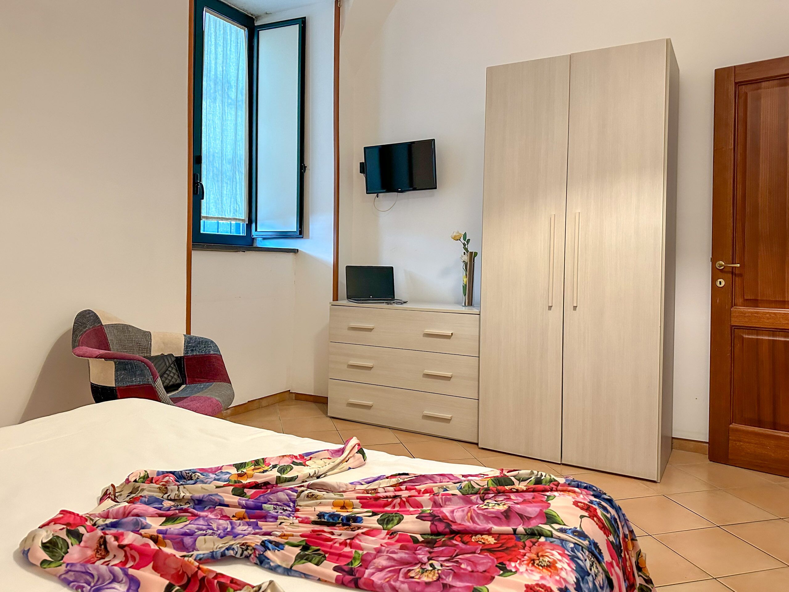 Une chambre à coucher avec un lit, une armoire, un bureau avec un ordinateur portable, une chaise et une fenêtre.