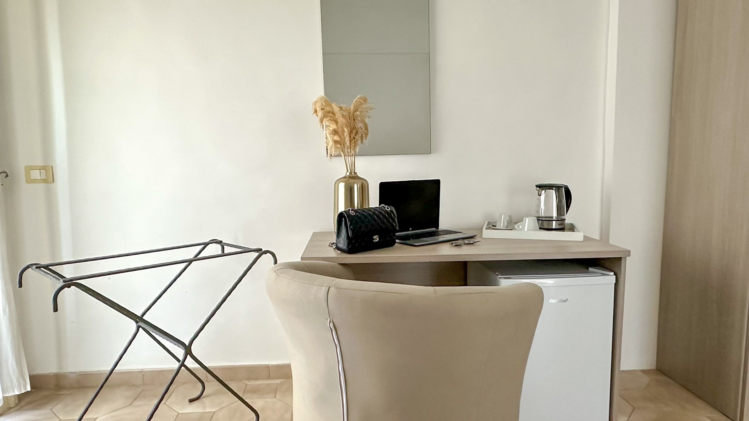 Un espacio de oficina moderno y minimalista con un escritorio, computadora portátil, cafetera y un jarrón decorativo.