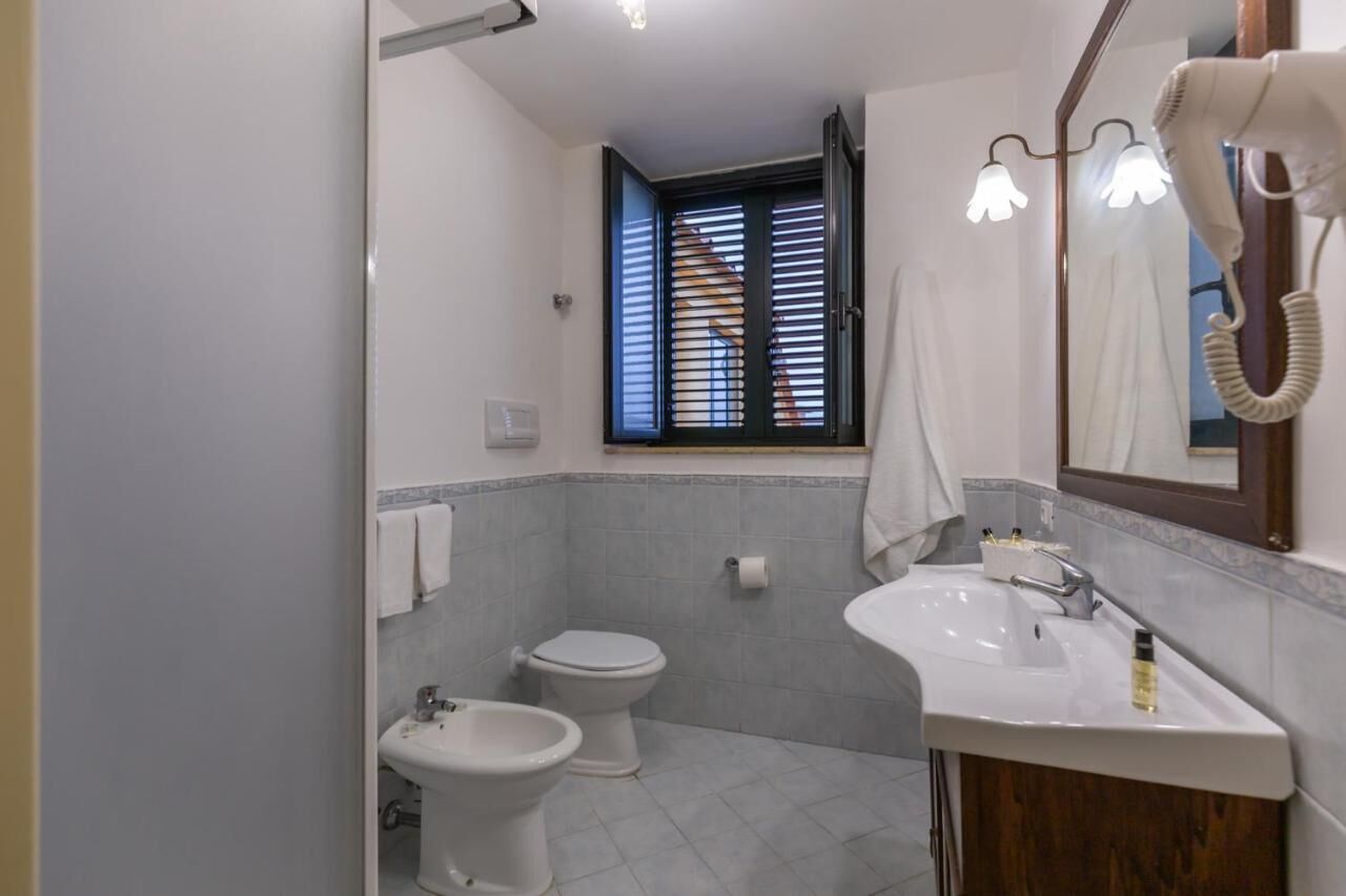 A bathroom with a toilet, bidet, sink, and a hairdryer mounted on the wall.