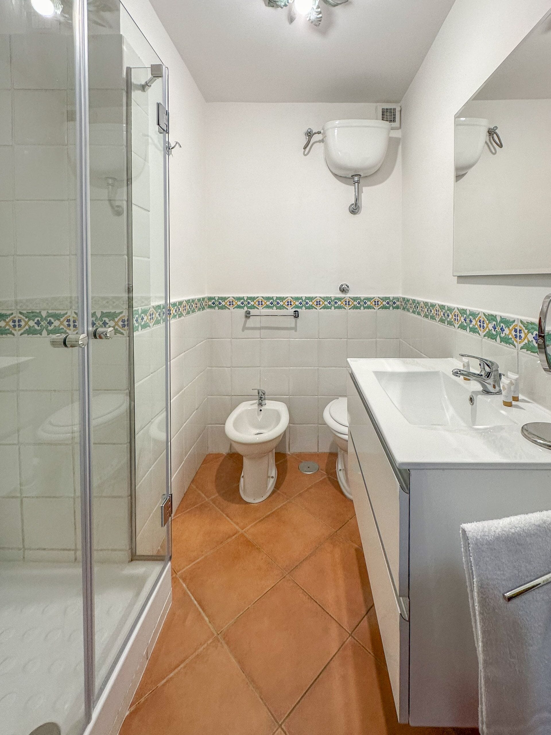 A bathroom with a glass shower enclosure, two toilets, a sink, and a mirror.