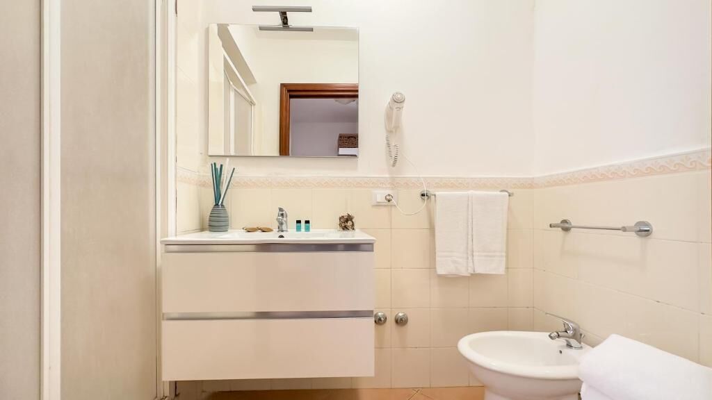Un bagno con lavandino, specchio, porta asciugamani e asciugacapelli.