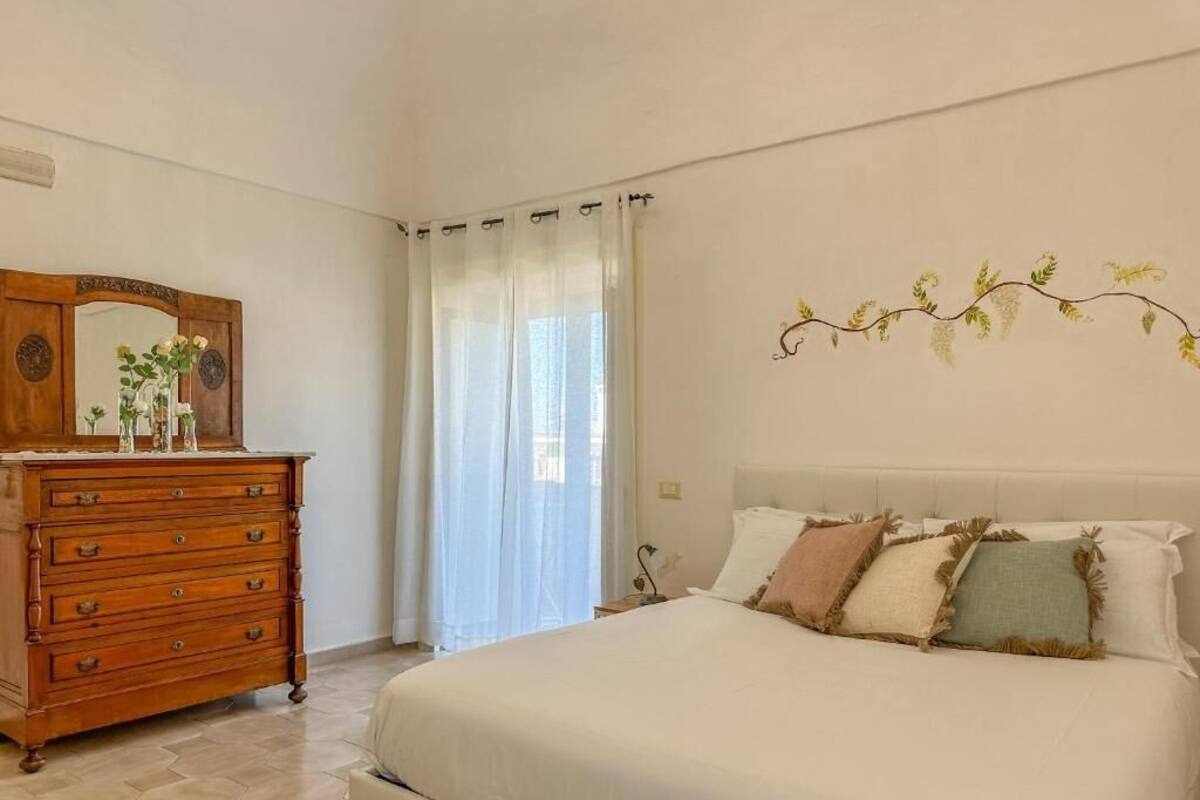 A bedroom with a bed, a wooden dresser, a mirror, and a window with curtains.