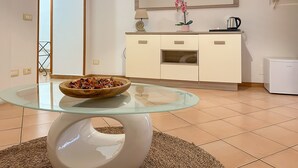 Una camera moderna con un tavolo con piano in vetro, una ciotola di legno, un armadietto bianco, uno specchio e un piccolo elettrodomestico bianco.