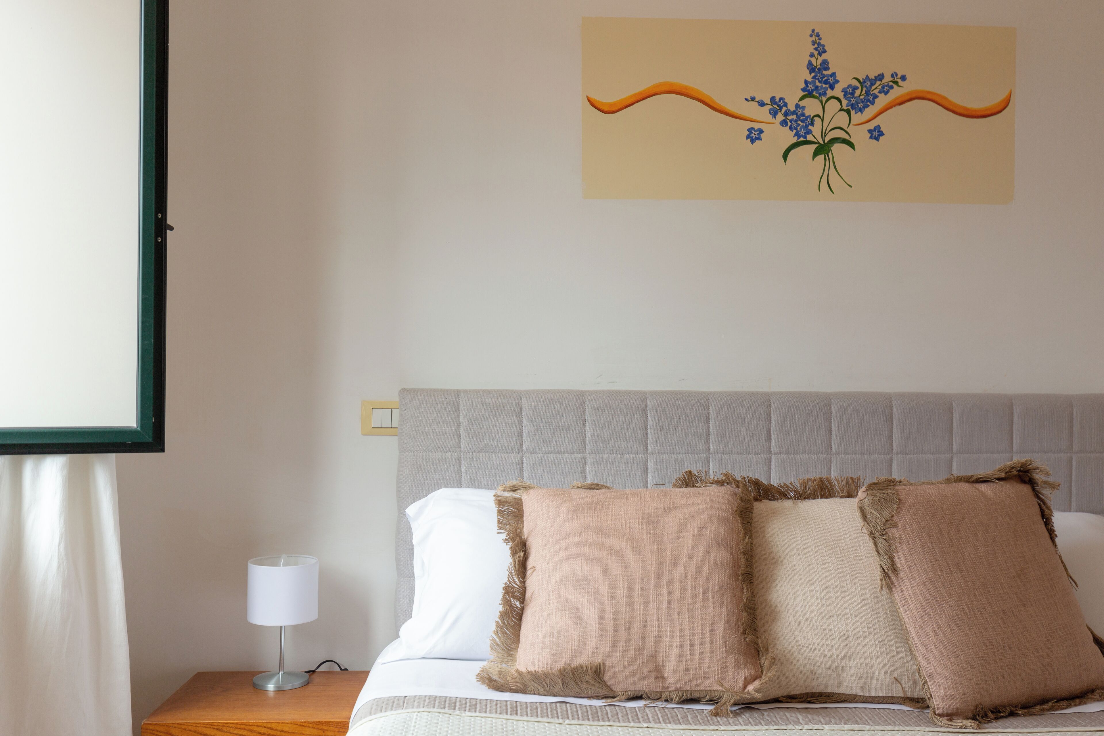 A neatly made bed with two pillows, a bedside lamp, and a framed artwork on the wall.