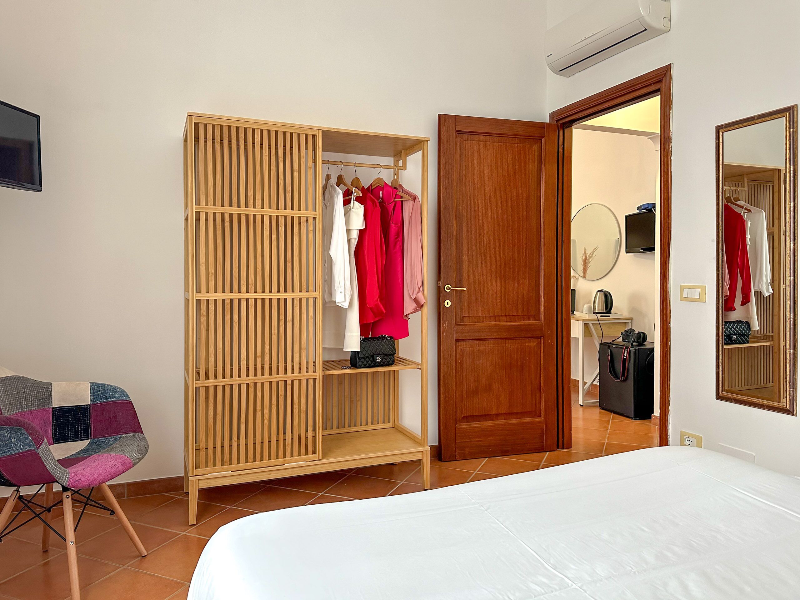 Un dormitorio con cama, armario de madera, una silla y un espejo.