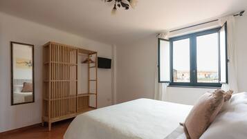 Una camera da letto con un letto, un armadio in legno, una televisione e una finestra con tende.