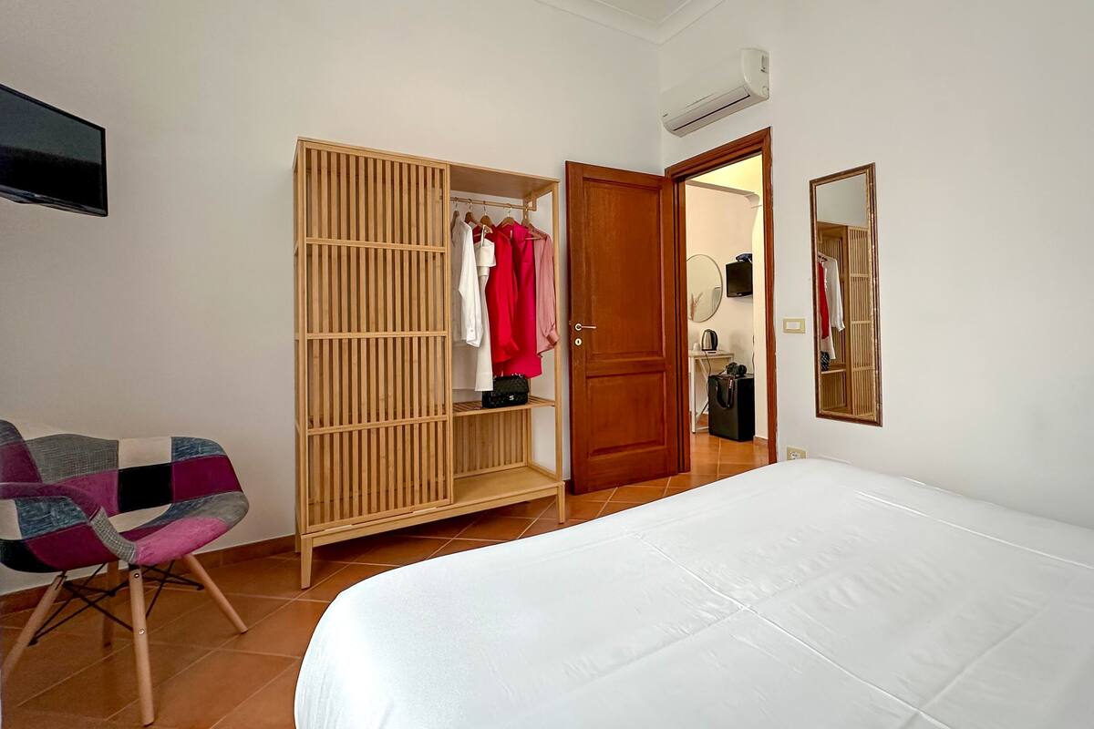 A bedroom with a bed, a wooden wardrobe, a chair, and a mirror.