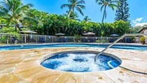 Un jacuzzi rodeado por una piscina de piedra con palmeras al fondo.