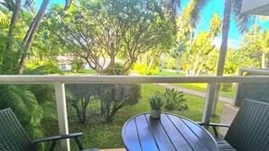 Ein Balkon mit rundem Tisch und zwei Stühlen, mit Blick auf einen gepflegten Garten mit verschiedenen Bäumen und einer Rasenfläche.