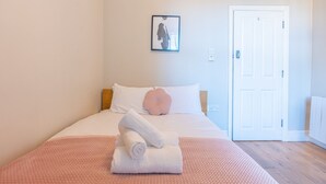 A neatly made bed with a pink blanket, a white pillow, and a rolled white towel on top. - Bloomfield 4 (Lancaster)