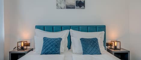 Una cama doble con cabecera color aguamarina, dos mesitas de noche con lámparas, y tres obras de arte en la pared sobre la cama.