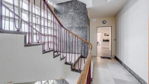 A staircase with a wooden handrail and red balusters, leading to a landing with a black marble wall and a door in the background.