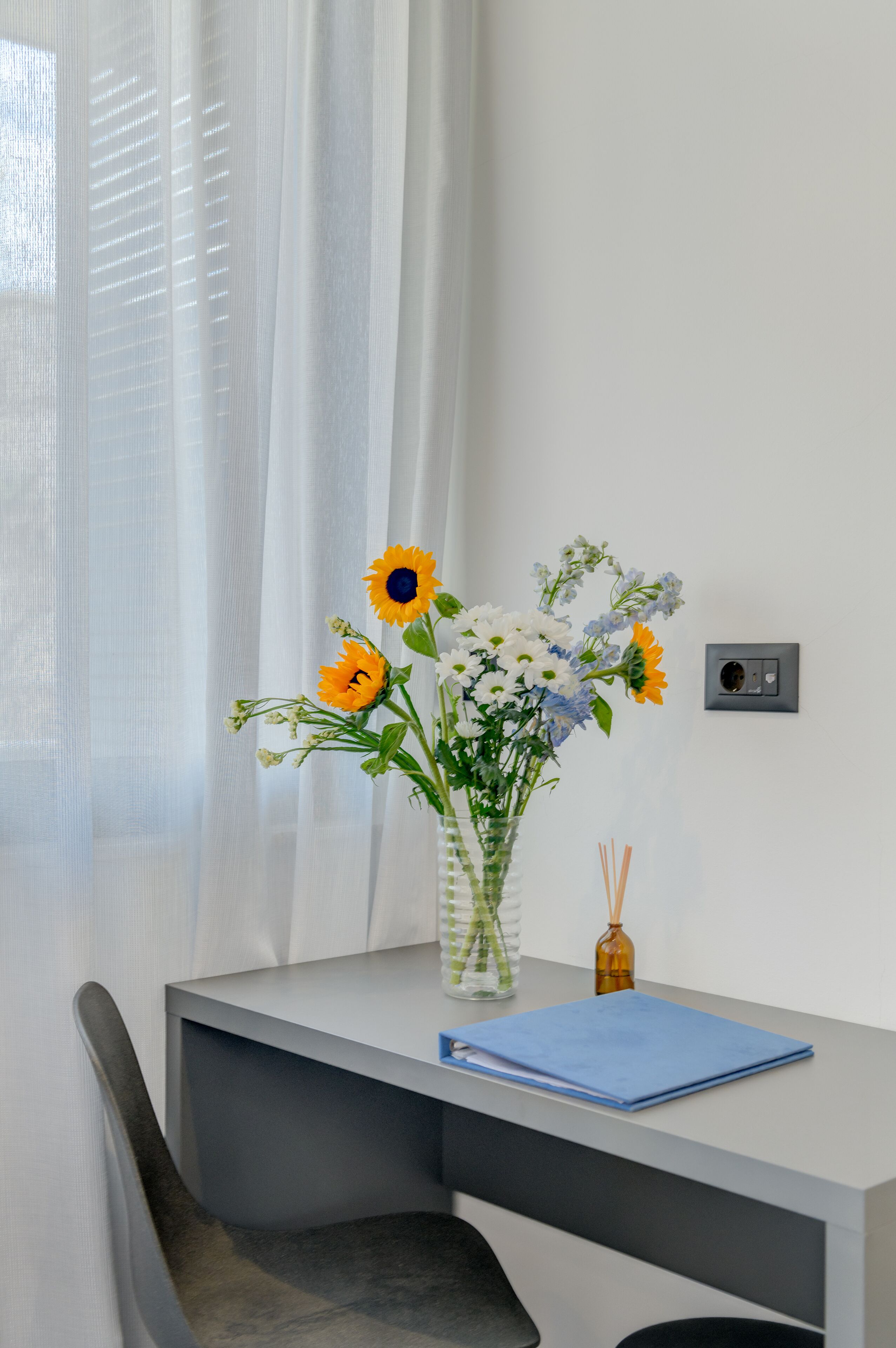 A modern desk with a vase of flowers, a blue notebook, and a diffuser.