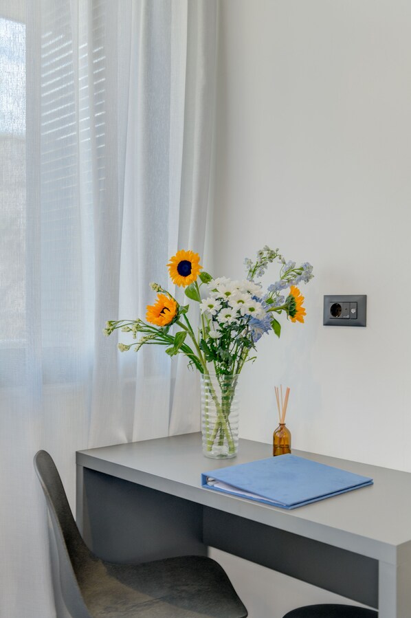 A modern desk with a vase of flowers, a blue notebook, and a diffuser.
