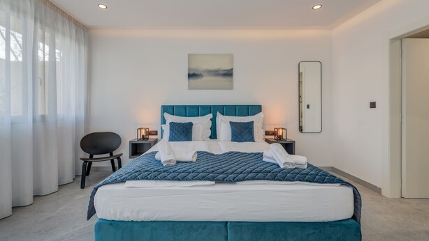 A modern bedroom with a large bed, a chair, bedside tables, and a painting on the wall.