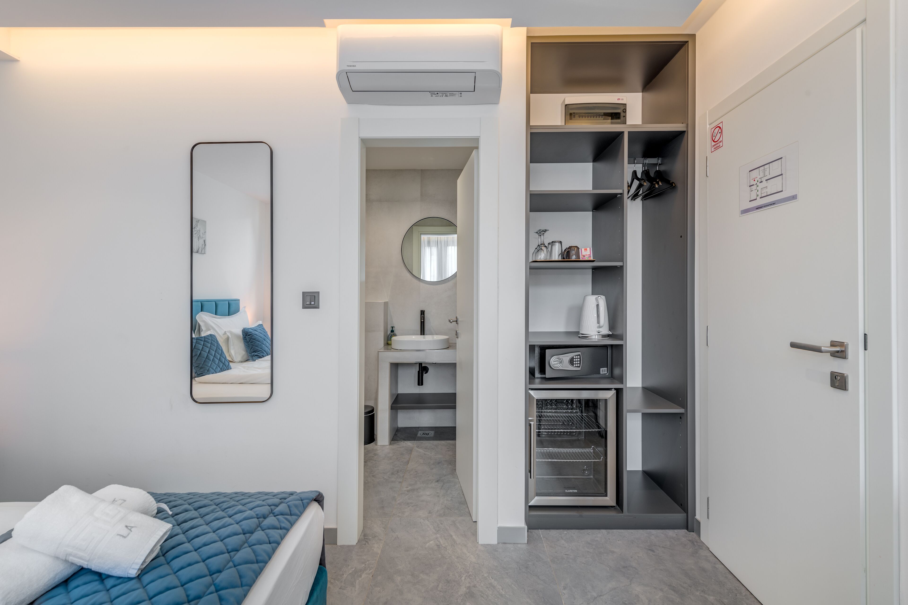 A hotel room with a bed, a mirror, a bathroom with a sink and toilet, a wardrobe, and a built-in oven.