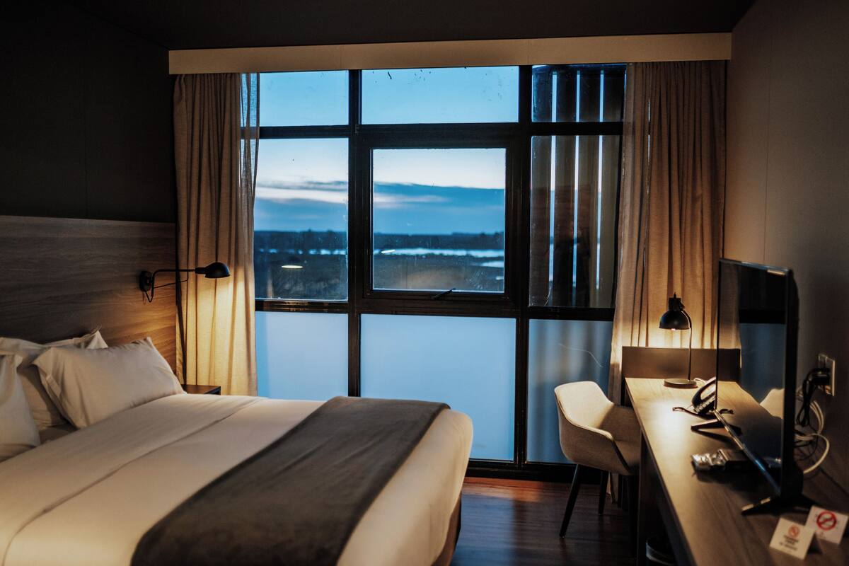 Une chambre d’hôtel avec une grande fenêtre, un lit, un bureau et une chaise.