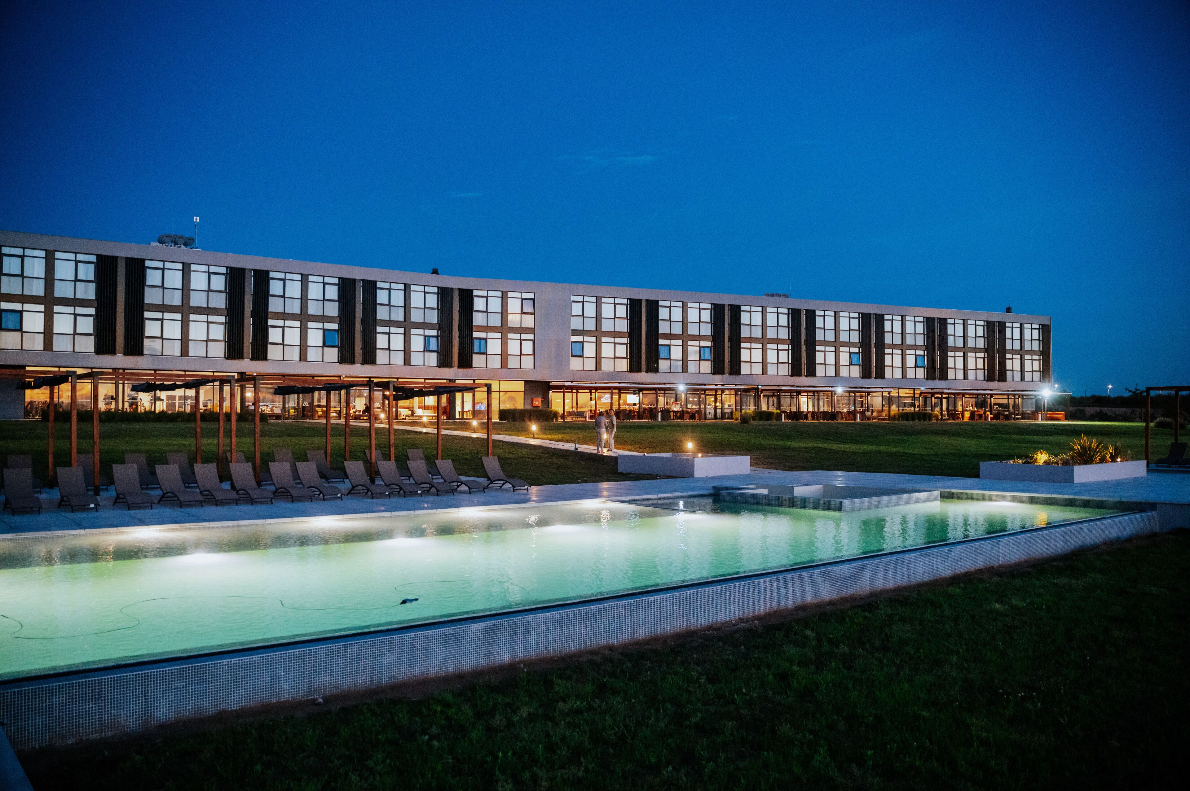 Un hôtel moderne doté d’une piscine, de chaises longues et d’un espace extérieur bien éclairé.