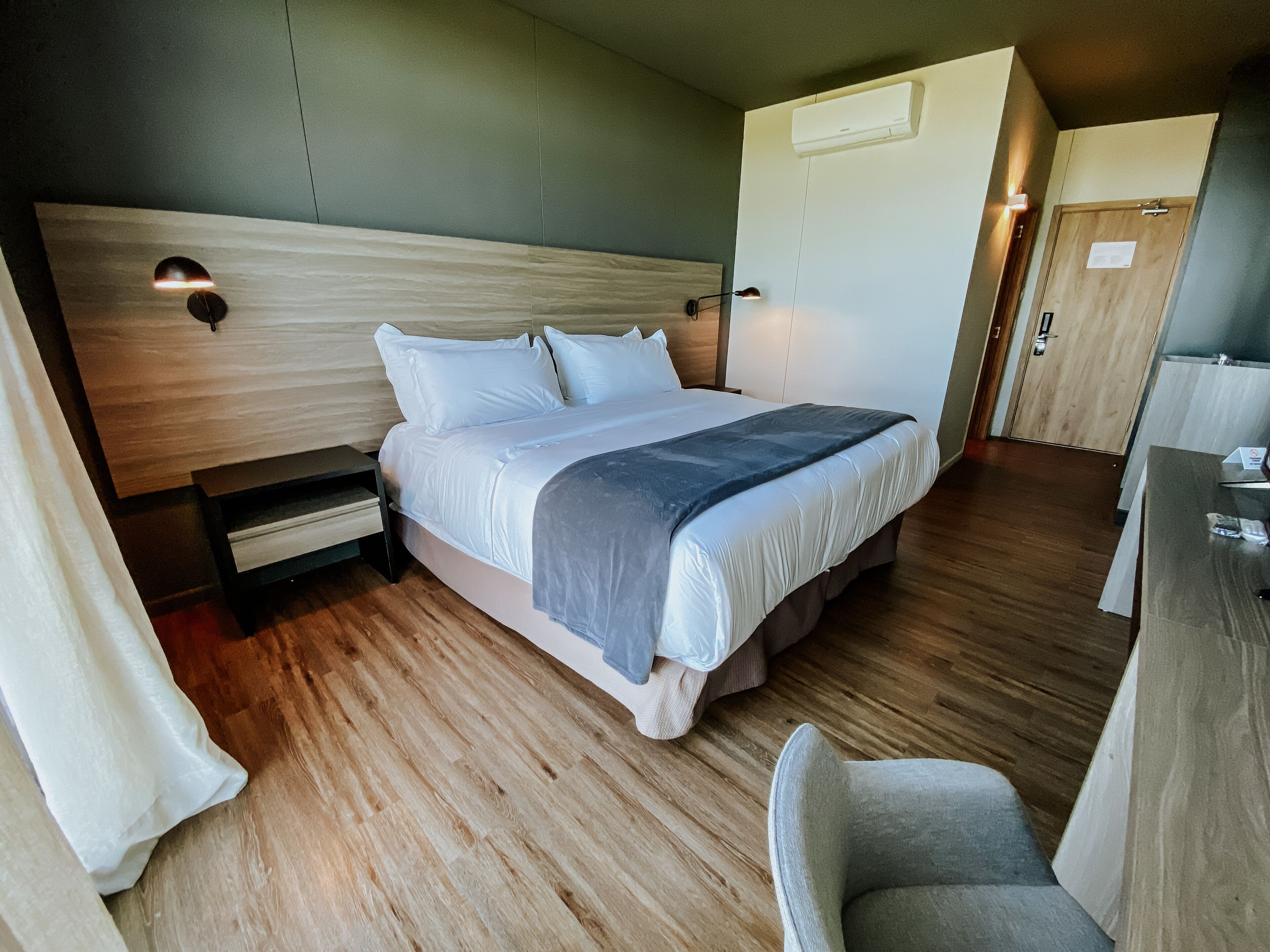 A modern hotel room with a large bed, wooden flooring, a desk, and a chair.