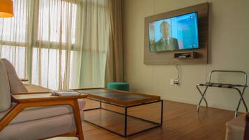 A modern living room with a wooden coffee table, a sofa, a teal ottoman, and a television mounted on the wall.