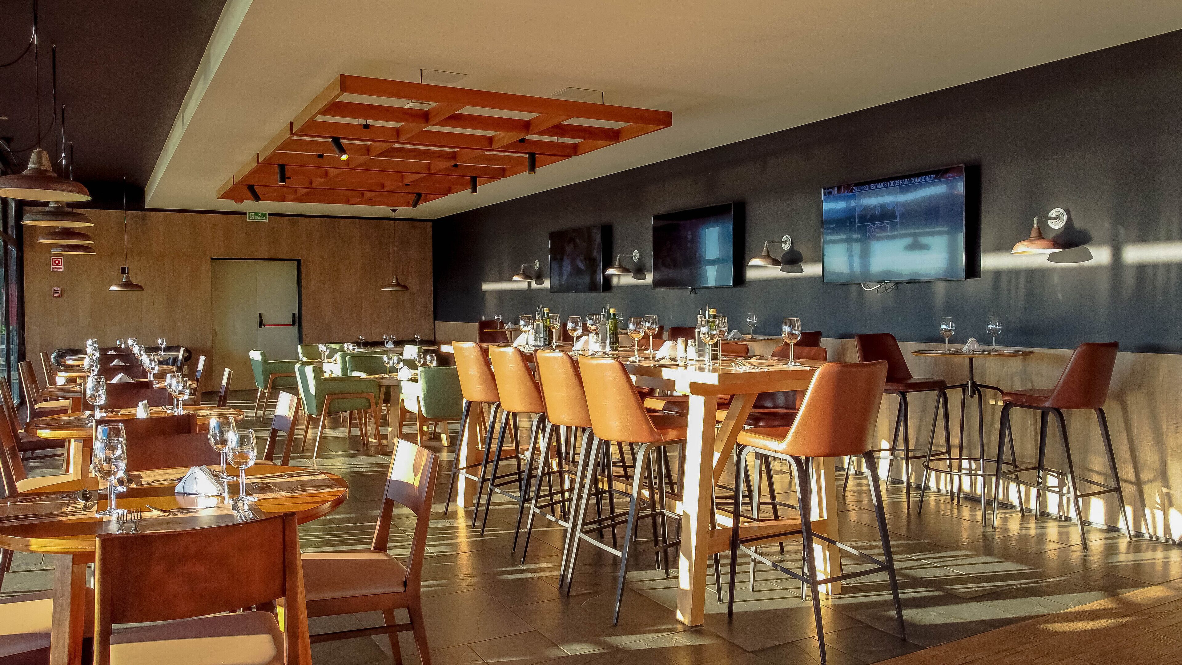 Un restaurante espacioso con numerosas mesas y sillas, vigas de madera en el techo y un diseño moderno.