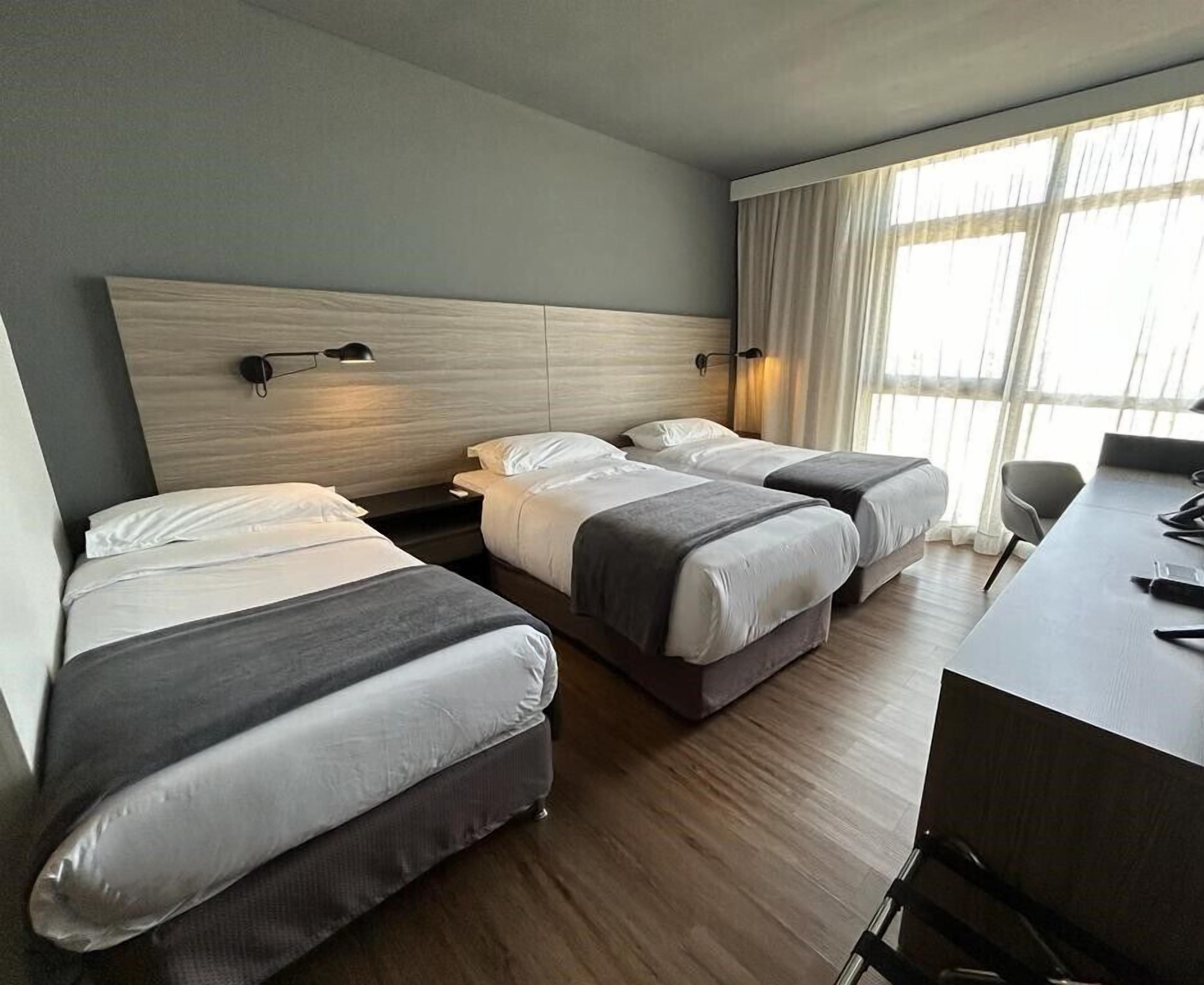 A hotel room with two single beds, a desk, and a chair.