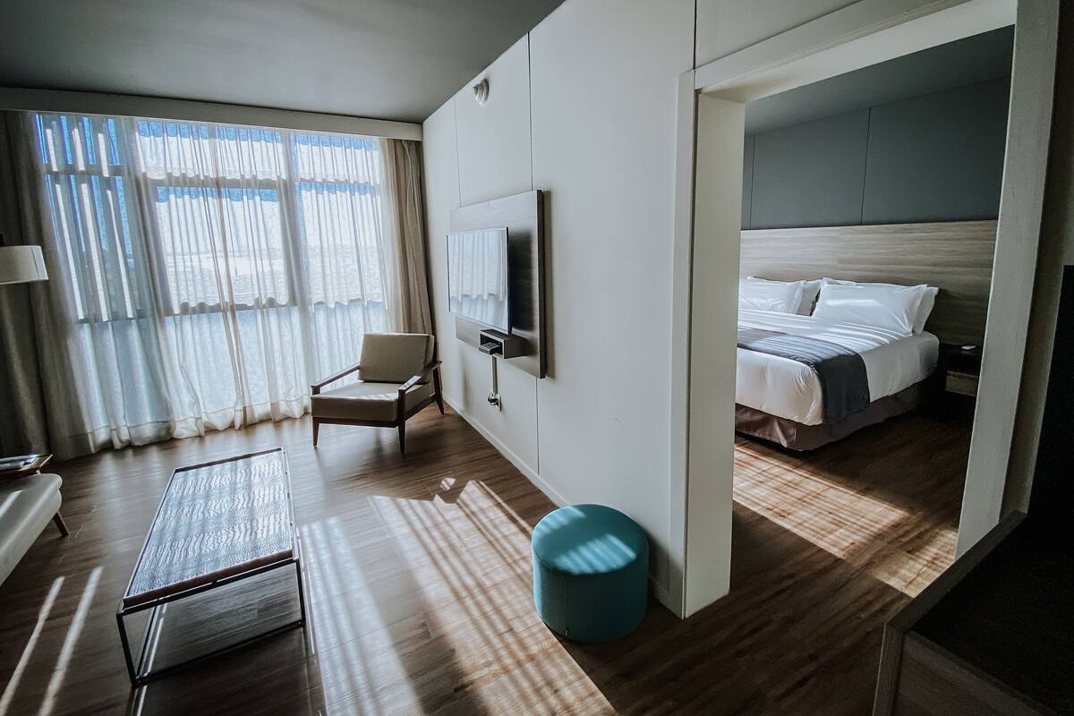 Une chambre d’hôtel moderne équipée d’un lit, d’un téléviseur fixé au mur, d’un coin salon avec un fauteuil et d’une petite table.