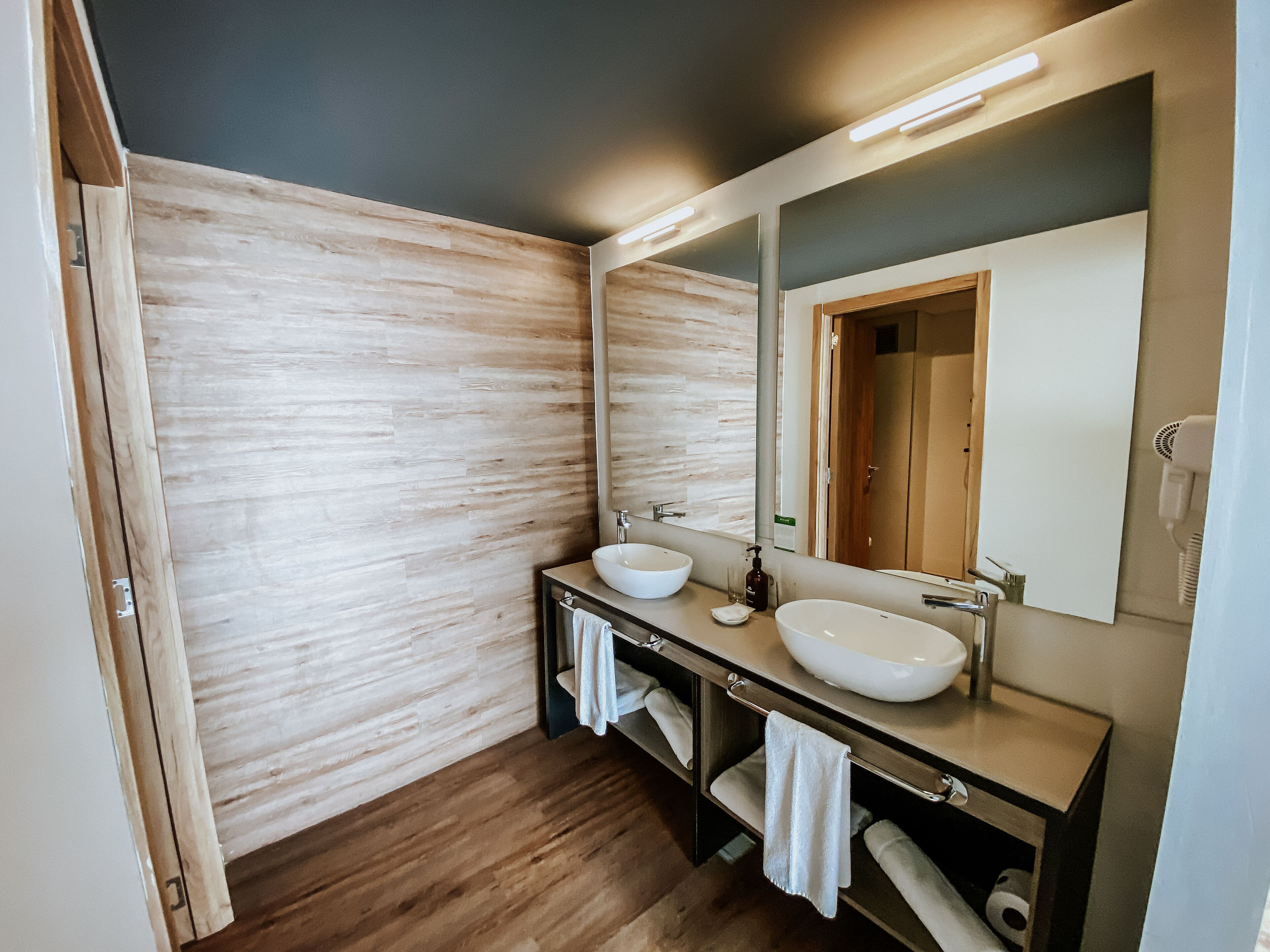 Un baño moderno con dos lavamanos, un espejo grande y suelo de madera.