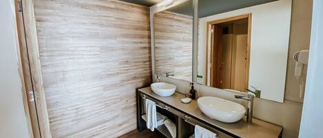Un baño moderno con dos lavamanos, un espejo grande y suelo de madera.