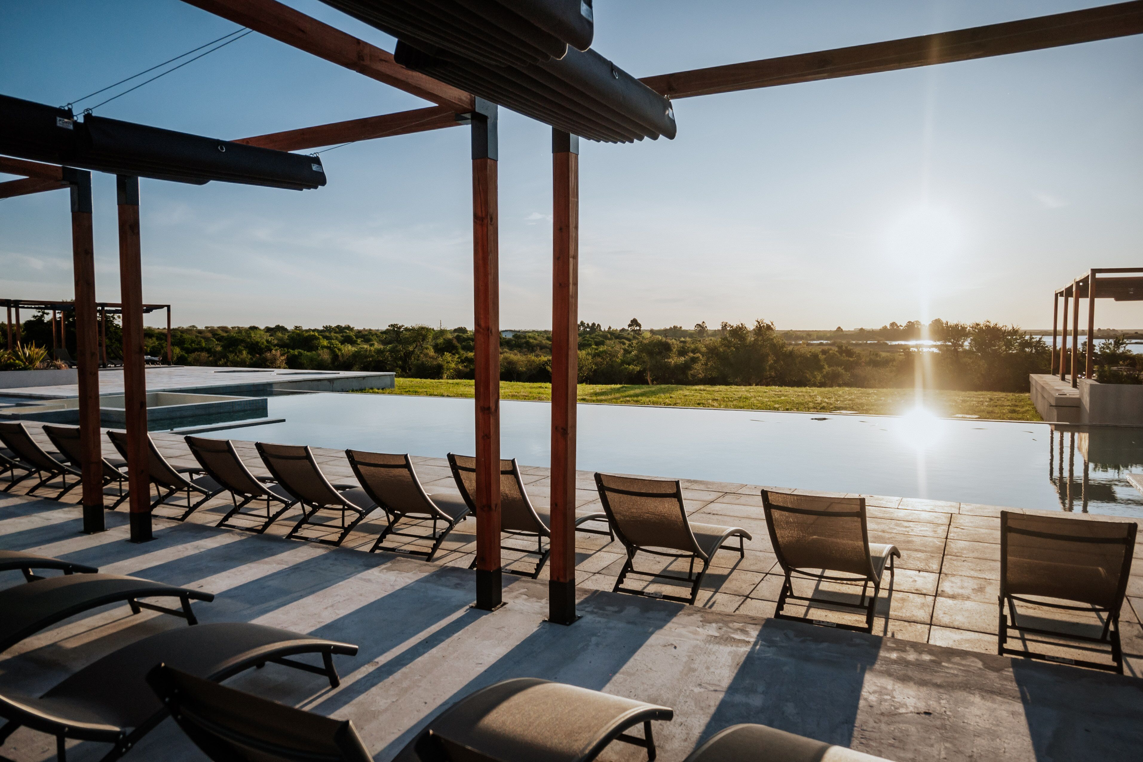 Un área junto a la piscina con sillones de descanso y una pérgola.